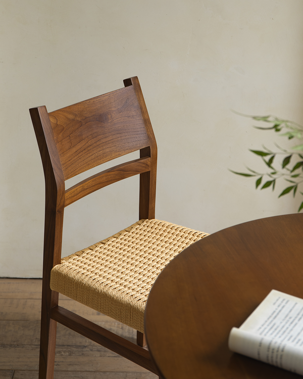 Close-up of Beam Chair with woven seat next to a round wooden table