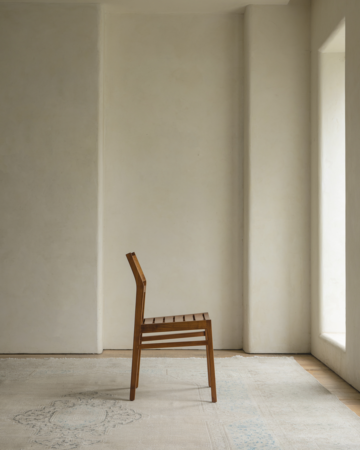 Beam Chair in profile view against a minimalist wall and patterned rug.