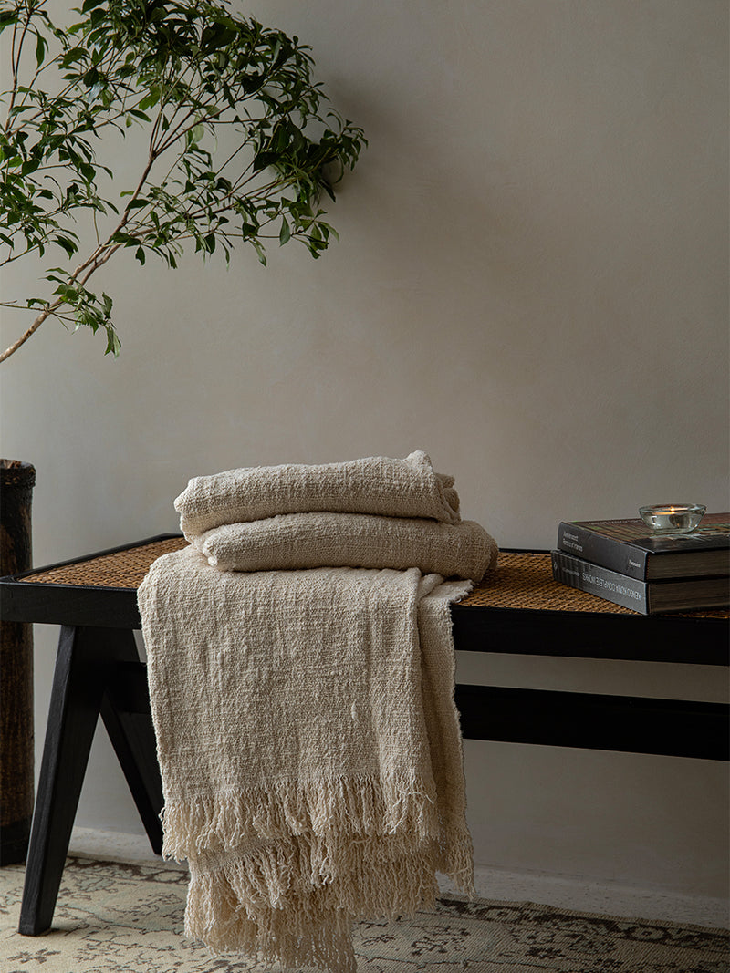 Cream cotton blankets stacked on black bench with decorative books and a plant