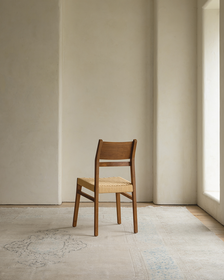 Profile view of Beam Chair with woven seat in minimalist room with natural light.