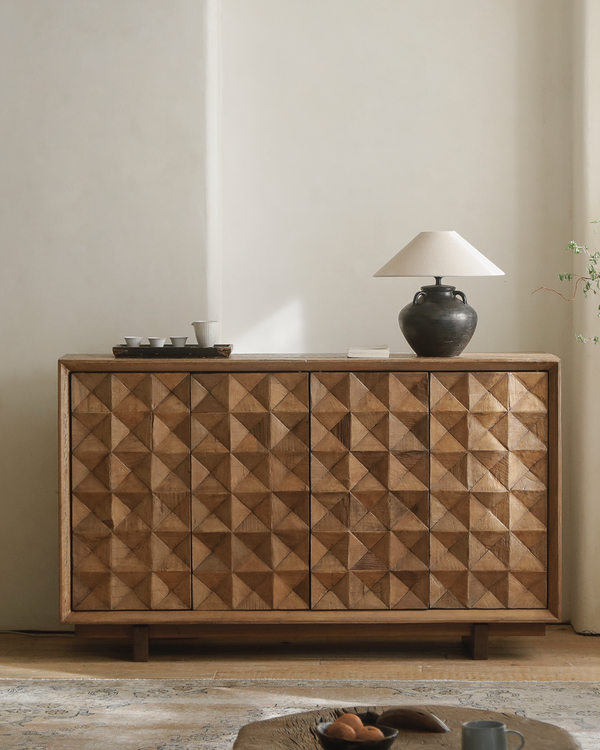 Bumpy sideboard with geometric design, lamp, and vase on top.