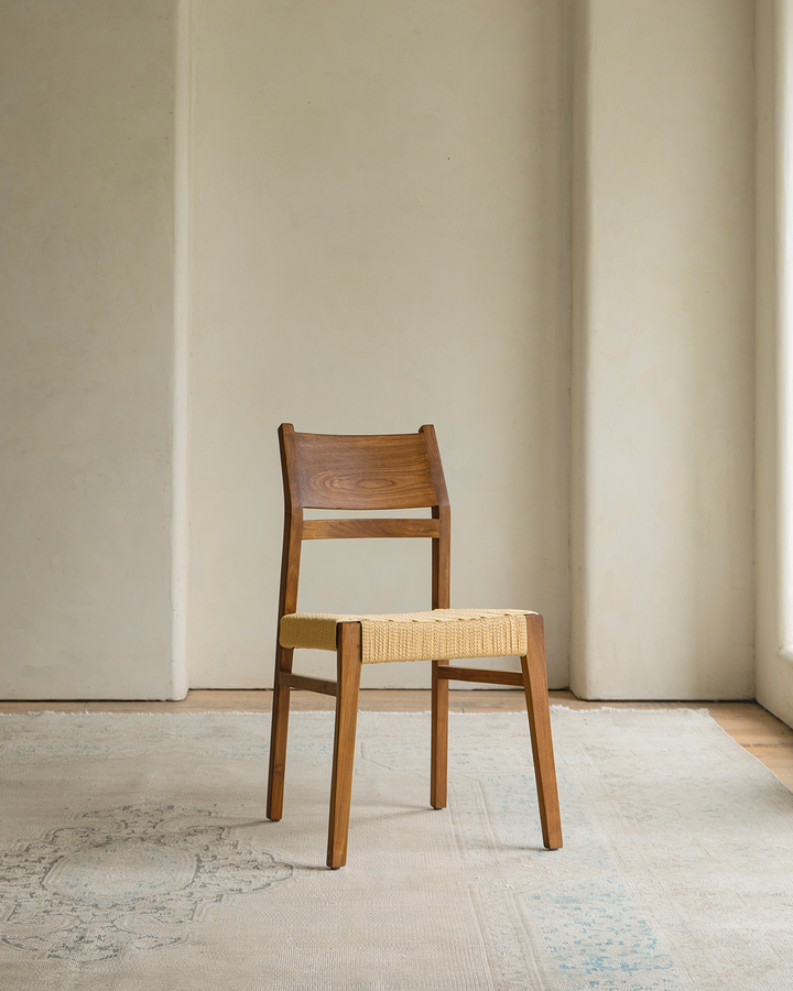 Beam Chair with woven seat in a bright minimalist room on a patterned rug.