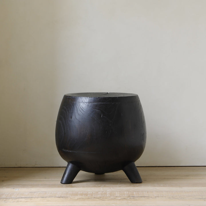 Round black wooden side table with three legs in a minimalist setting.