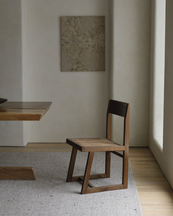 Chandigarh Box Chair with natural wood frame and handwoven seat next to minimalist table.